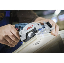 Une personne utilise une scie circulaire Bosch pour couper une planche de bois, avec de la sciure visible.