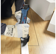 Personne avec des gants de protection utilisant un découpeur-ponceur sans fil Bosch Professional pour couper un sol en bois.