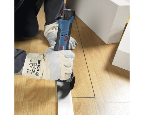 Personne avec des gants de protection utilisant un découpeur-ponceur sans fil Bosch Professional pour couper un sol en bois.