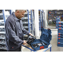 Un homme insère un plateau avec perceuse-visseuse Bosch et chargeur dans un coffret Bosch L-BOXX dans un atelier organisé.