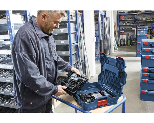 Un homme insère un plateau avec perceuse-visseuse Bosch et chargeur dans un coffret Bosch L-BOXX dans un atelier organisé.