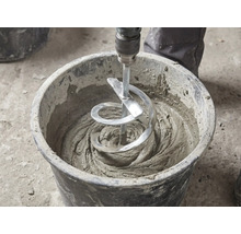 Un mélangeur à spirale mélange du mortier gris dans un seau de chantier noir.