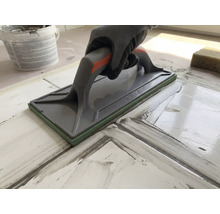 Main avec gant de protection utilisant un platoir à jointer pour jointoyer des carreaux.