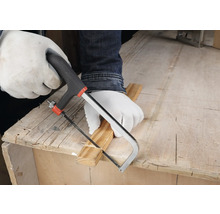 Person mit weissen Schutzhandschuhen schneidet eine Holzleiste mit einer kleinen Handsäge auf einer hölzernen Werkbank.