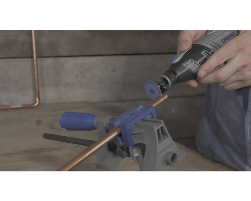 Un tube en cuivre fixé dans un étau est coupé avec un outil multifonction Dremel et un disque à tronçonner.