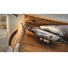 Outil multifonction Dremel 4250 coupant une vis dans une caisse en bois avec projection d'étincelles.