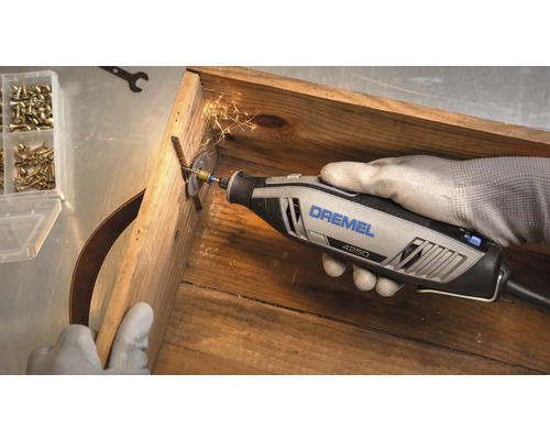 Outil multifonction Dremel 4250 coupant une vis dans une caisse en bois avec projection d'étincelles.