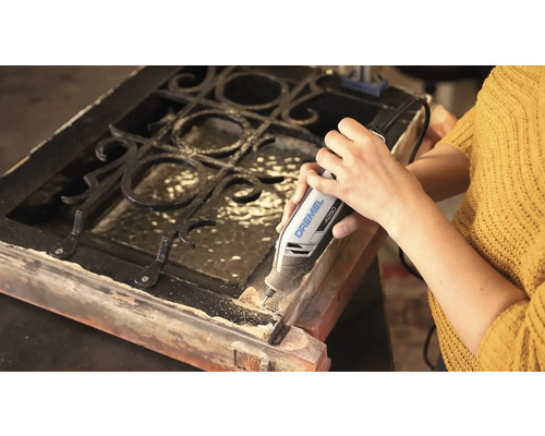 Une personne utilise un outil multifonction Dremel 4250 pour travailler sur un cadre en bois avec une grille métallique.