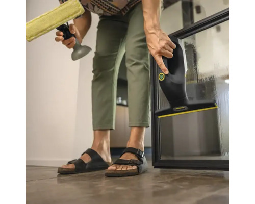 Une personne nettoie une vitre avec un nettoyeur de vitres et un flacon pulvérisateur avec raclette.