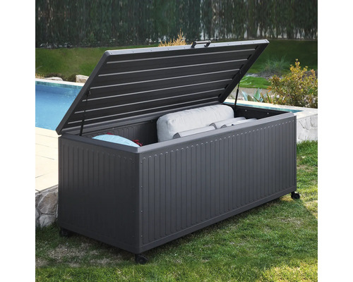 Coffre de jardin en métal gris foncé avec couvercle ouvert et roulettes, rempli de coussins, au bord d'une piscine.