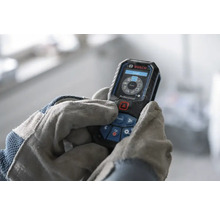 Télémètre laser Bosch Professional utilisé par des mains avec gants de travail, écran numérique avec fonctions de mesure.