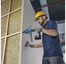 Professionnel fixant une plaque de plâtre avec une visseuse à plaque de plâtre à batterie et chargeur sur une structure isolée.