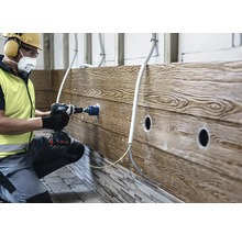 Un artisan perce une ouverture dans un revêtement mural à l'aspect bois avec une perceuse-visseuse sans fil et une scie cloche.