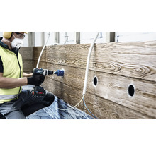 Artisan utilisant une perceuse-visseuse sans fil avec scie cloche pour percer un panneau mural avec aspect bois sur un chantier.