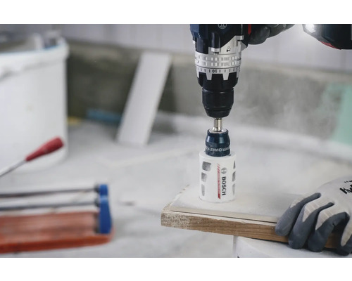 Perceuse-visseuse Bosch avec scie-cloche diamantée perçant un trou dans un carreau de céramique blanc.