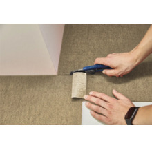 Une personne découpe un revêtement de sol texturé en feutre avec un cutter.