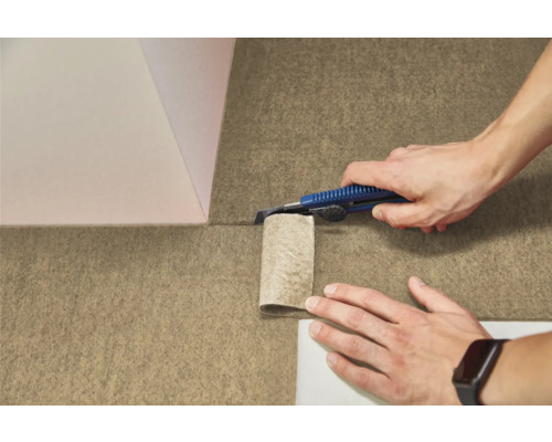 Une personne découpe un revêtement de sol texturé en feutre avec un cutter.