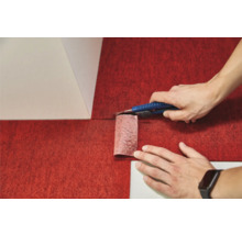 Une personne découpe une moquette rouge avec un cutter.