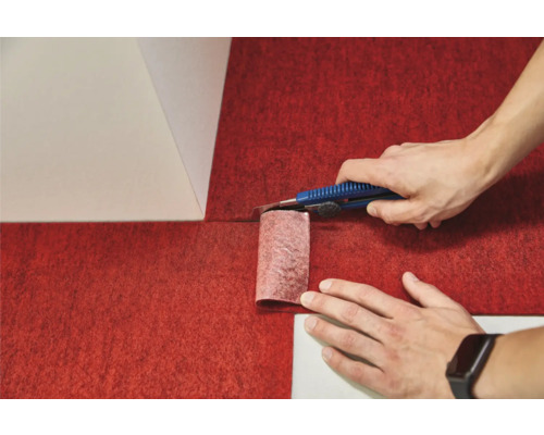 Une personne découpe une moquette rouge avec un cutter.