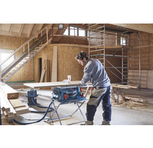 Un artisan utilise une scie sur table Bosch avec aspirateur sur un chantier pour couper un panneau en bois.