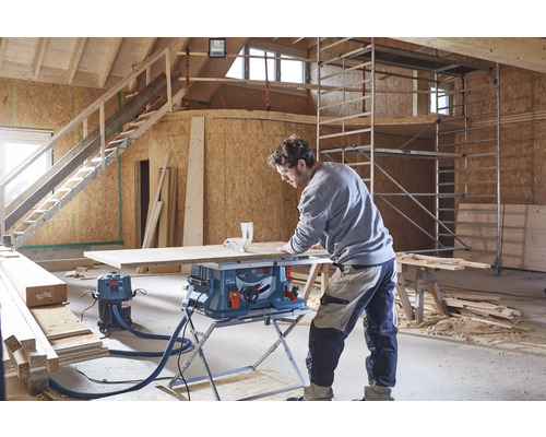 Un artisan utilise une scie sur table Bosch avec aspirateur sur un chantier pour couper un panneau en bois.