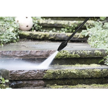 Ein Hochdruckreiniger entfernt Moos von Steinstufen im Aussenbereich mit einem kräftigen Wasserstrahl.