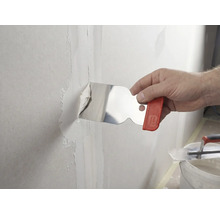 Une main applique de l'enduit sur un joint de mur à l'aide d'un couteau à enduire en acier inoxydable.