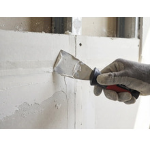 Hand mit Arbeitshandschuh trägt mit einem Rautner Malerspachtel Spachtelmasse auf ein Bewehrungsband an einer Trockenbauwand auf.