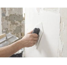 Une main lisse de l'enduit blanc sur un mur à l'aide d'un lisseur en plastique.