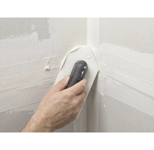 Main utilisant une truelle d angle pour lisser l enduit dans un angle intérieur de plaques de plâtre.