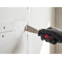 Hand mit Arbeitshandschuh nutzt eine Rautner Malerspachtel zum Verfugen von Gipskartonplatten.