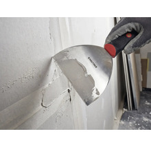 Main gantée utilisant une spatule Rautner pour appliquer de l enduit sur un mur.