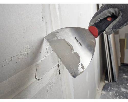 Main gantée utilisant une spatule Rautner pour appliquer de l enduit sur un mur.