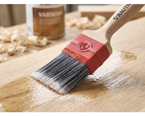 RAUTNER Pinsel trägt Klarlack auf eine Holzoberfläche auf. Mit Synthetikborsten, Holzgriff und roter Zwinge. Im Hintergrund eine Dose Lack.
