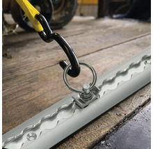 Rail d'arrimage avec raccord à anneau métallique et crochet de sangle pour la sécurisation du chargement sur un sol en bois.