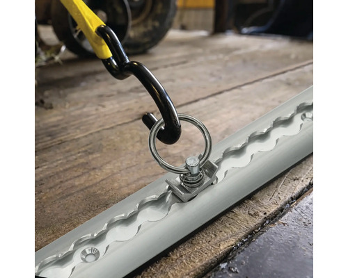 Rail d'arrimage avec raccord à anneau métallique et crochet de sangle pour la sécurisation du chargement sur un sol en bois.