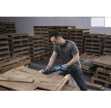 Homme utilisant une scie sabre Bosch Professional sur une palette en bois dans un entrepôt lumineux.