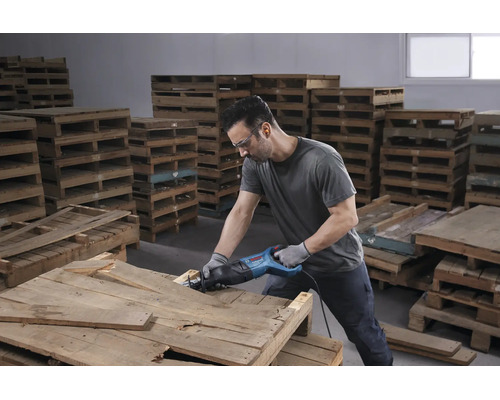 Homme utilisant une scie sabre Bosch Professional sur une palette en bois dans un entrepôt lumineux.