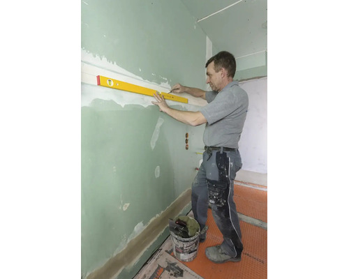 Handwerker nutzt eine Wasserwaage und einen Bleistift, um eine waagrechte Linie an einer grünen Gipskartonwand zu markieren.