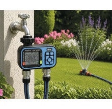 Bewässerungscomputer mit for_q Logo am Gartenwasserhahn montiert, zwei Schläuche angeschlossen, Rasensprenger bewässert helle Wiese im Hintergrund.