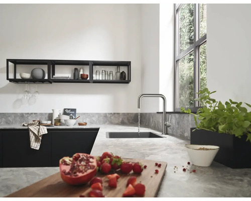 Cuisine moderne avec plan de travail gris clair aspect pierre, évier noir et robinet de cuisine en forme de U en acier inoxydable.