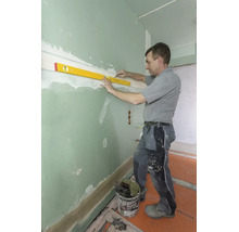 Handwerker nutzt eine Wasserwaage und einen Bleistift, um eine waagrechte Linie an einer grünen Gipskartonwand zu markieren.