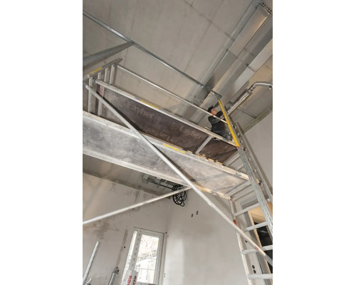 Handwerker auf einem Layher Fahrgerüst bei der Installation an einer Betondecke im Rohbau.