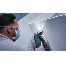 Artisan portant des lunettes de protection et un masque respiratoire sciant une découpe dans un panneau blanc avec un outil multifonction
