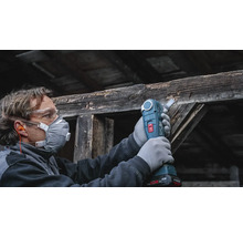 Artisan portant un équipement de protection utilisant un outil multifonction sans fil pour scier une ancienne poutre en bois.