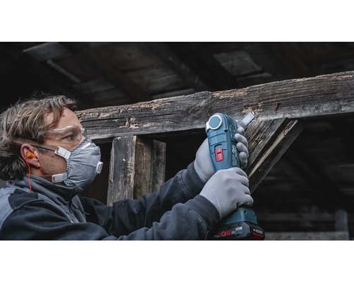 Artisan portant un équipement de protection utilisant un outil multifonction sans fil pour scier une ancienne poutre en bois.