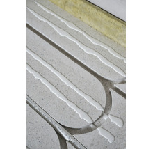 Installation d'un chauffage au sol avec des plaques grises, de la colle blanche, un tube composite et des bandes isolantes.
