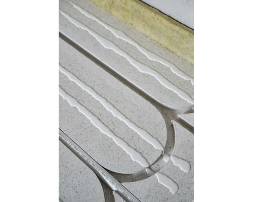 Installation d'un chauffage au sol avec des plaques grises, de la colle blanche, un tube composite et des bandes isolantes.
