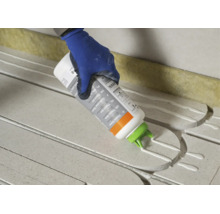 Main avec gant de travail appliquant de la colle thermique sur des plaques isolantes.