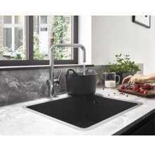 Cuisine moderne avec un robinet chromé en forme de L versant de l'eau dans un bac noir dans un évier noir sur un plan de travail marbré.